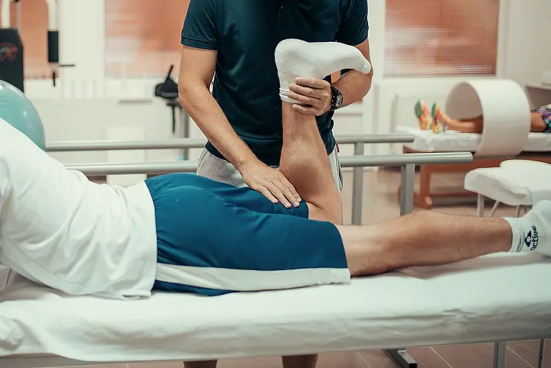 A physiotherapist mobilising a patient’s leg on a treatment table